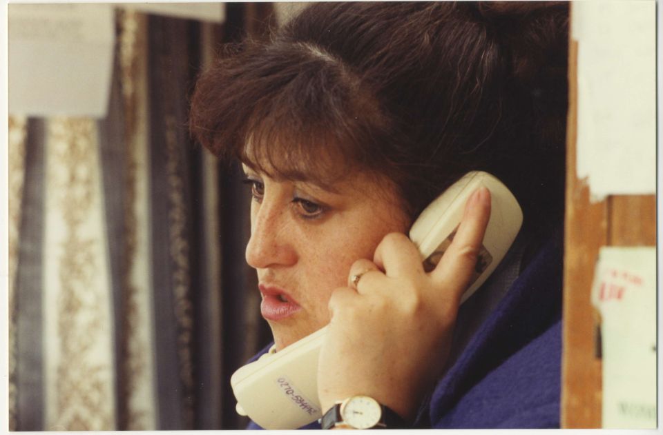 Colour photograph of Rose Hunter inside the Trentham caravan, holding a phone to her ear as if in conversation. She is looking to the left, away from the camera.